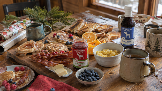 Holiday breakfast board with pancakes, eggs, bacon, fruit, jam, and whole fruit syrup
